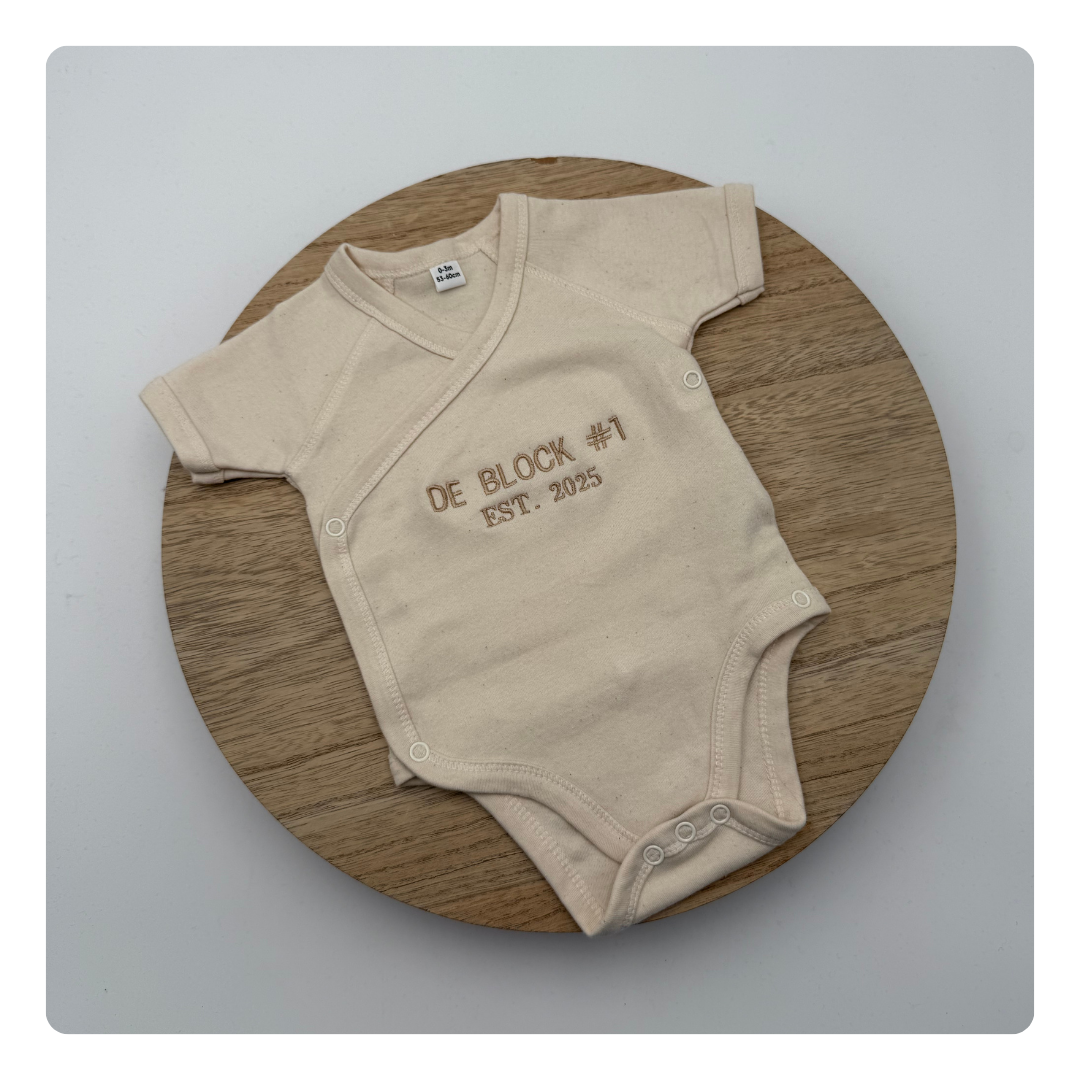 Witte babyromper met geborduurde tekst voor zwangerschapsaankondiging
