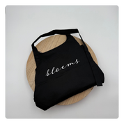 Zwart keukenschort met geborduurde tekst “Bloems” op de borst – gepersonaliseerd door Mbroidery